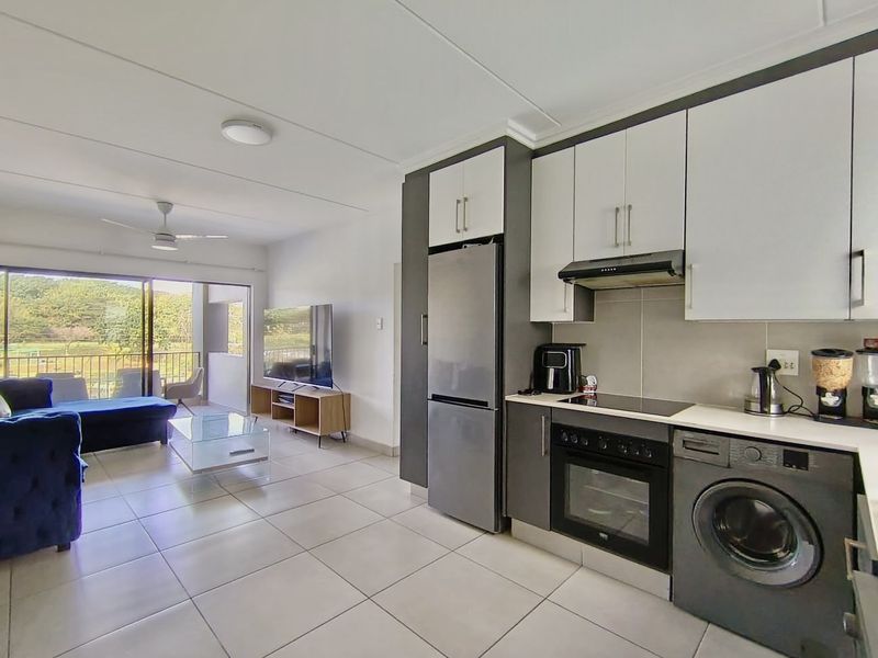 Modern open-plan living area featuring a contemporary kitchen with built-in appliances, tiled flooring, and seamless access to a balcony with scenic views.