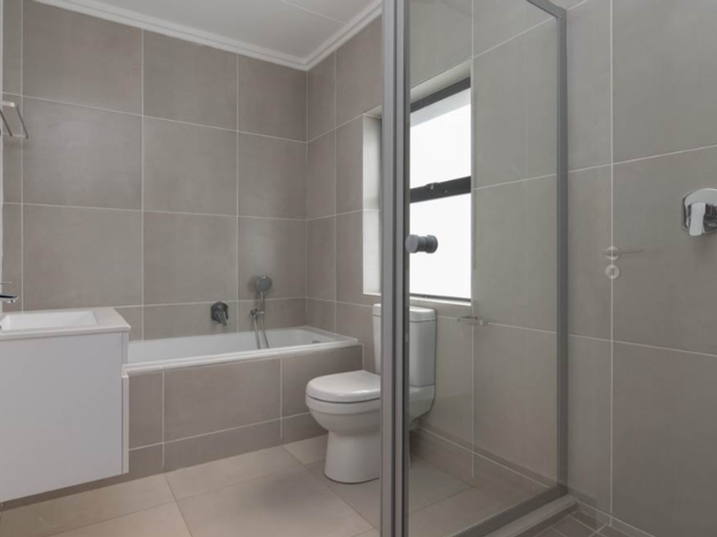 Modern bathroom featuring a built-in bathtub, separate glass-enclosed shower, vanity basin, and neutral floor-to-ceiling tiling.