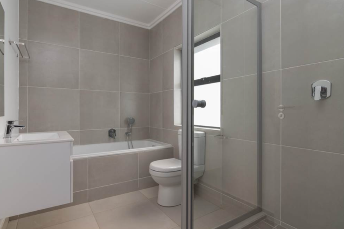 Modern bathroom featuring a built-in bathtub, separate glass-enclosed shower, vanity basin, and neutral floor-to-ceiling tiling.