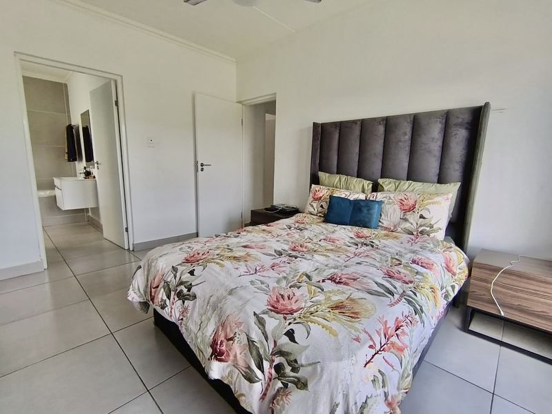 A well-maintained bedroom featuring neutral tiled flooring, a ceiling fan, and direct access to an en-suite bathroom.