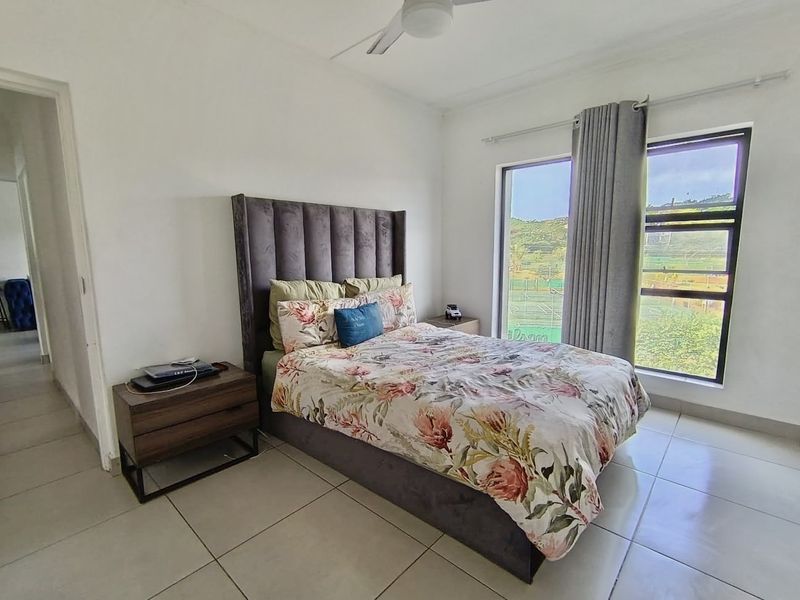 A bright bedroom featuring large windows with natural light, tiled flooring, and a ceiling fan, offering a comfortable and functional living space.