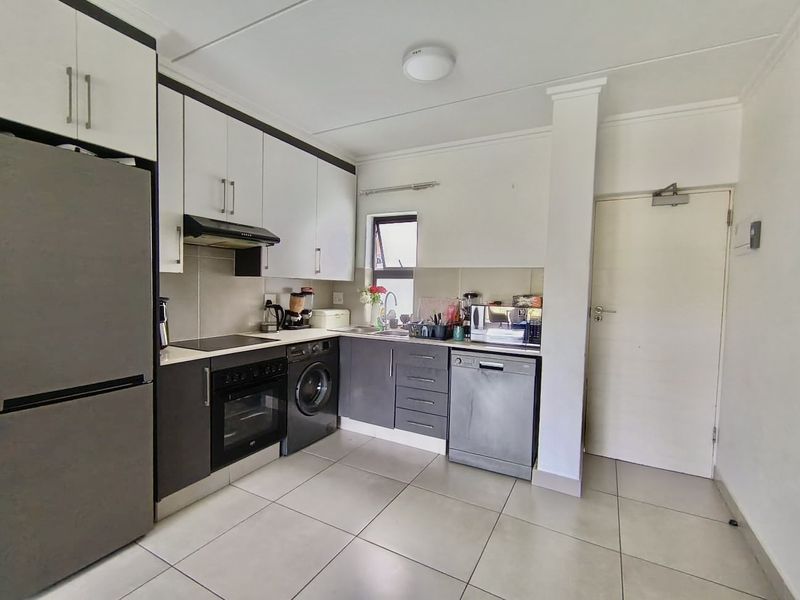 A functional kitchen featuring modern two-tone cabinetry, integrated appliances, tiled flooring, and a practical layout with ample storage and workspace.