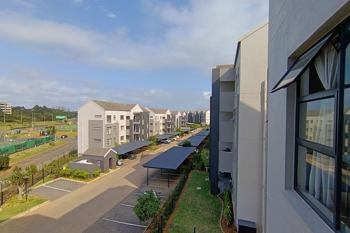 Elevated view of the apartment complex grounds, featuring paved parking areas, covered carports, and well-maintained communal lawn spaces.