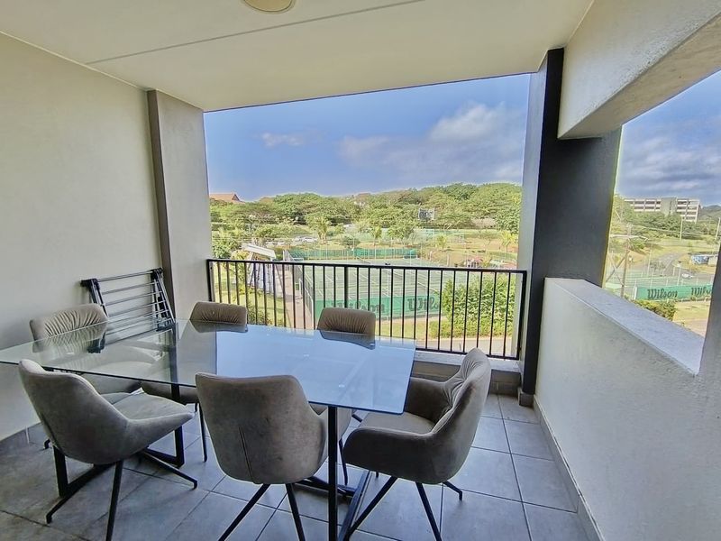 A covered balcony featuring tiled flooring and a metal balustrade, offering an open view of the surrounding recreational facilities.