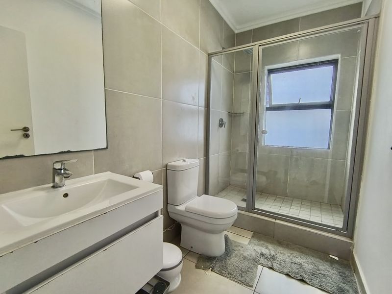 A functional bathroom featuring a vanity cabinet, toilet, and a glass-enclosed shower with neutral wall and floor tiling.