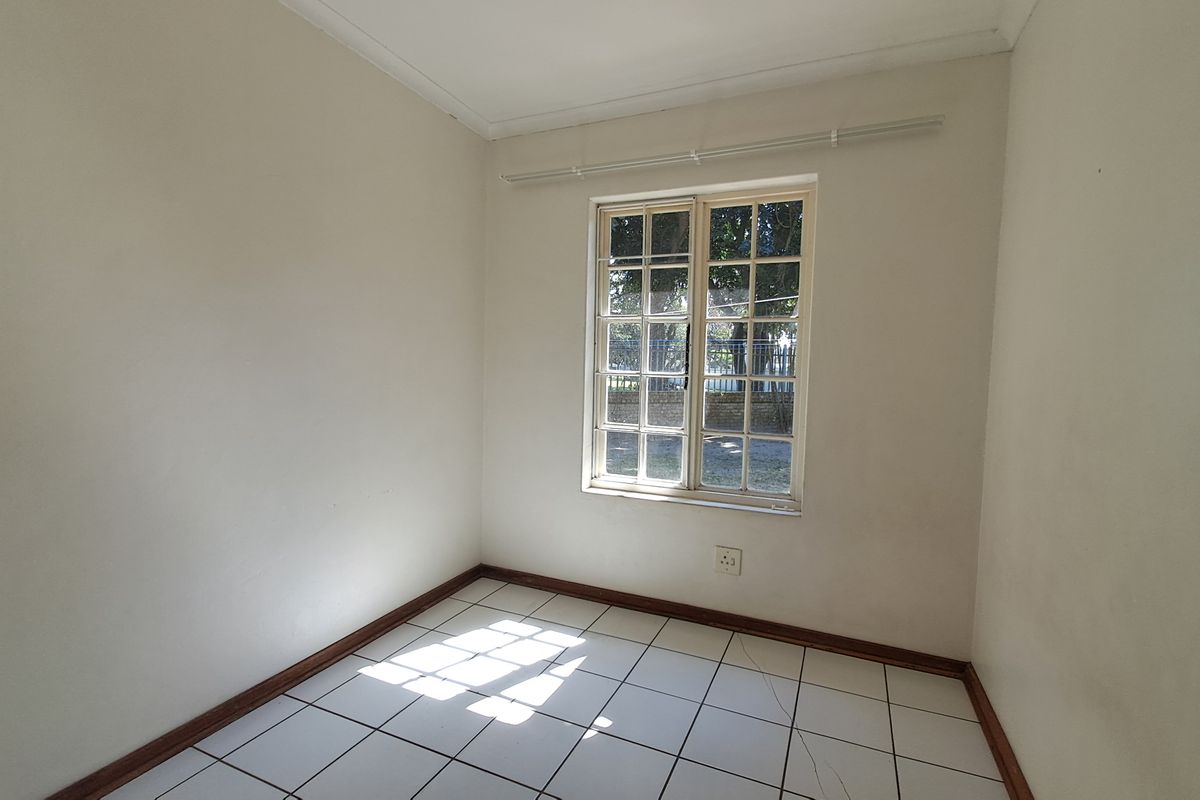 A vacant bedroom featuring white walls, tiled flooring, and a window with security bars, offering a blank canvas for personalization.