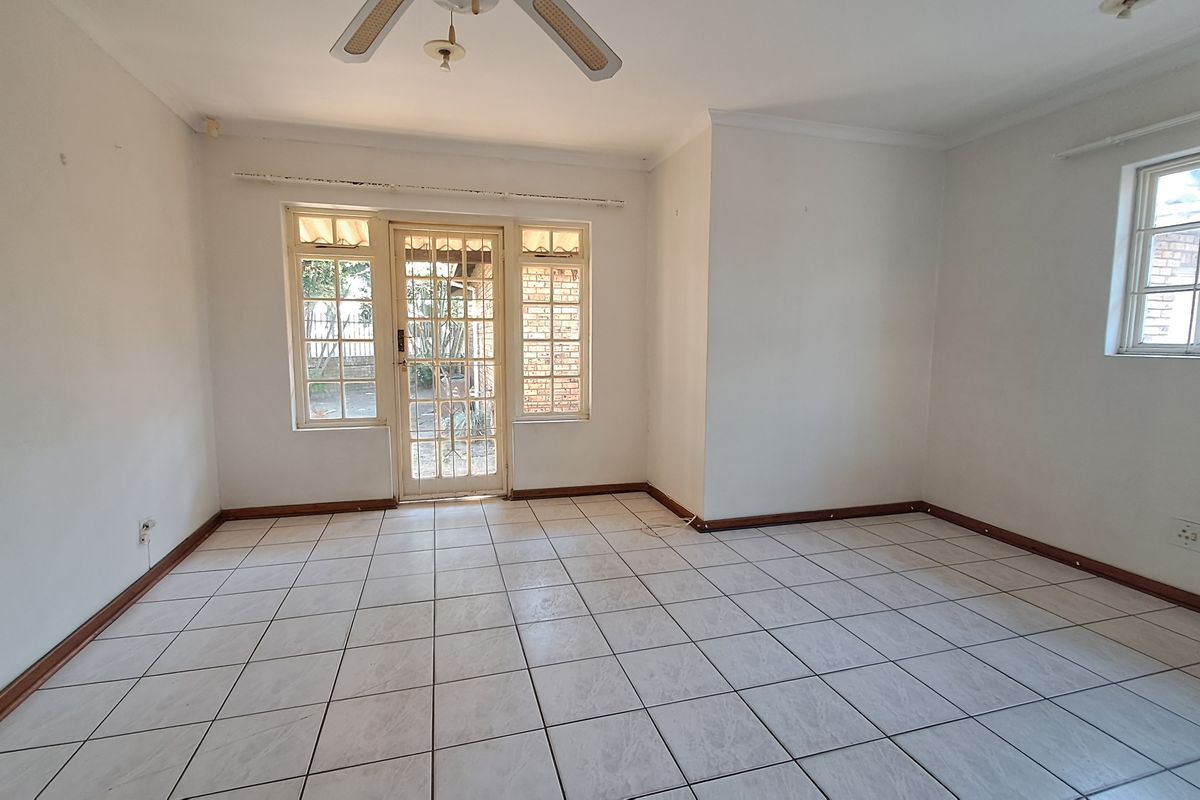 An empty, light-filled living room featuring neutral tiled flooring, a ceiling fan, and direct access to the exterior through a timber-framed glass door.