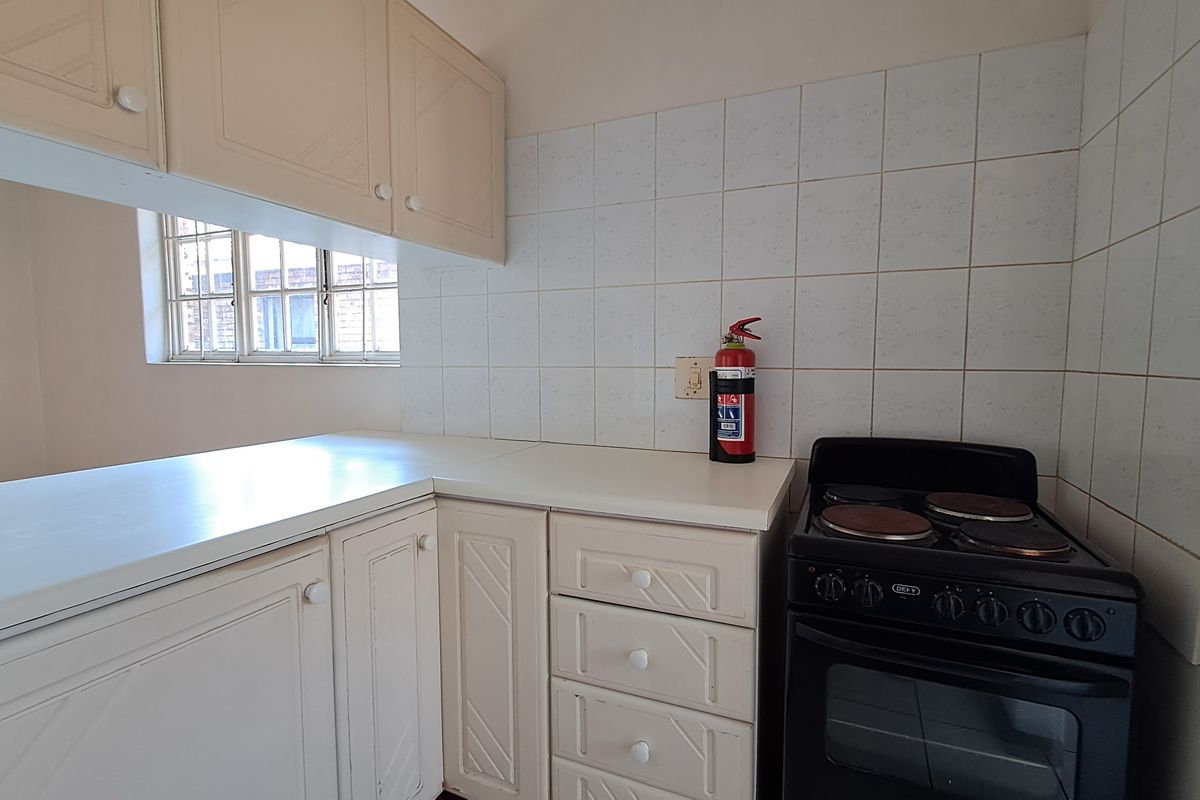 A functional kitchen featuring white built-in cabinetry, laminate countertops, a tiled backsplash, and a freestanding electric stove with security bars on the window.