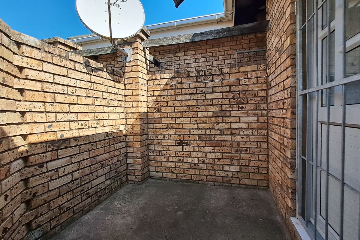 A private, enclosed rear courtyard featuring exposed brick walls, a concrete patio surface, and a secure metal gate entrance.