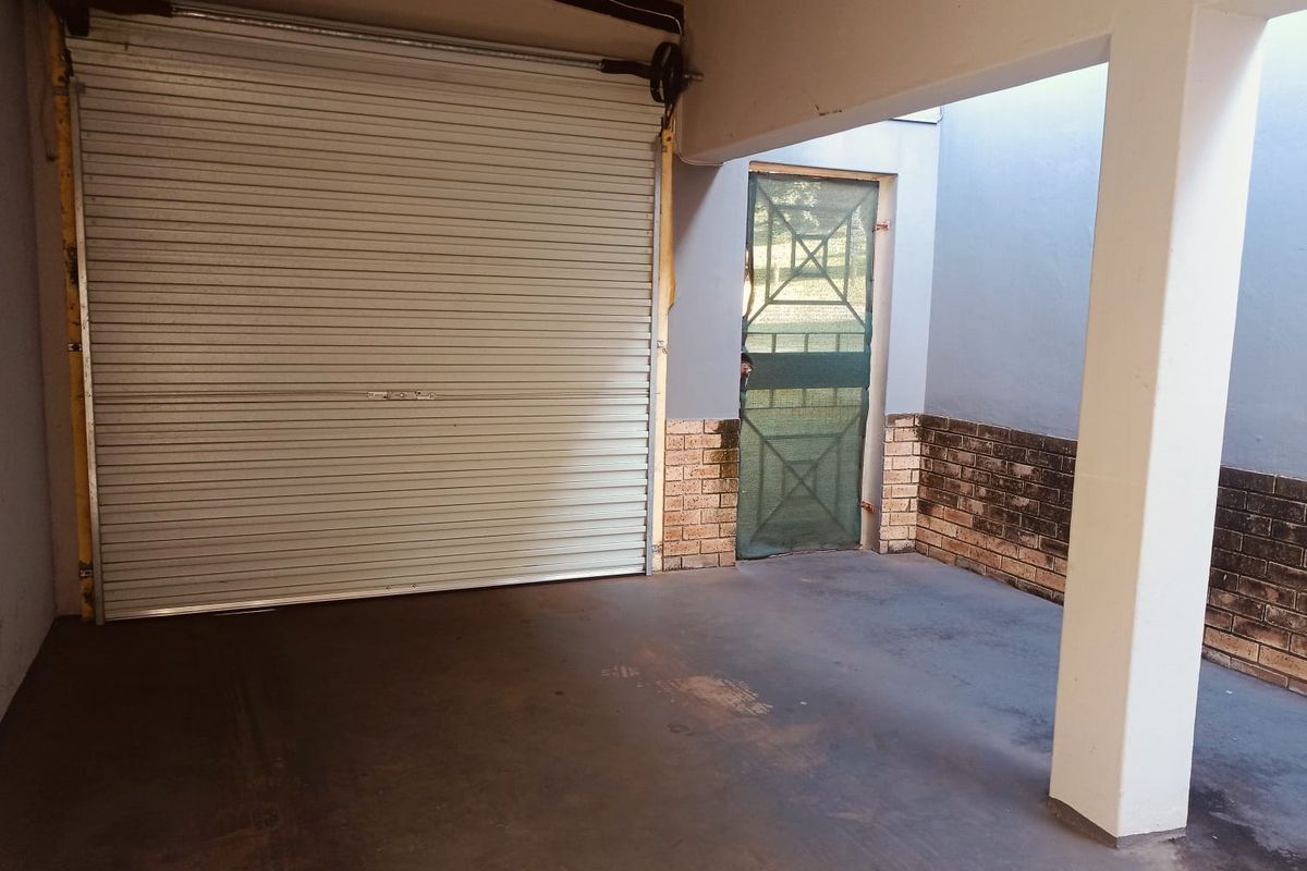 A functional garage space featuring a roller shutter door, concrete flooring, and a side security gate with brick-accented walls.