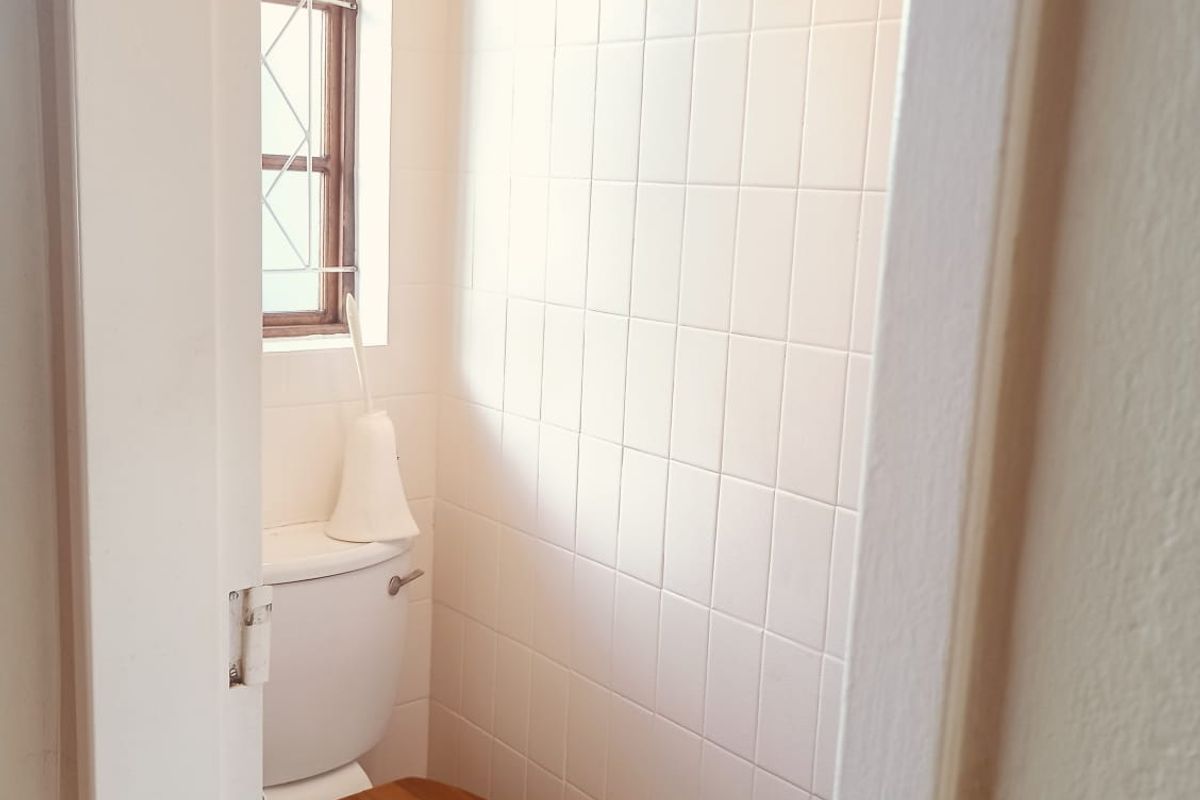 A compact bathroom featuring white wall tiles, tiled flooring, and a standard toilet with a window providing natural light.