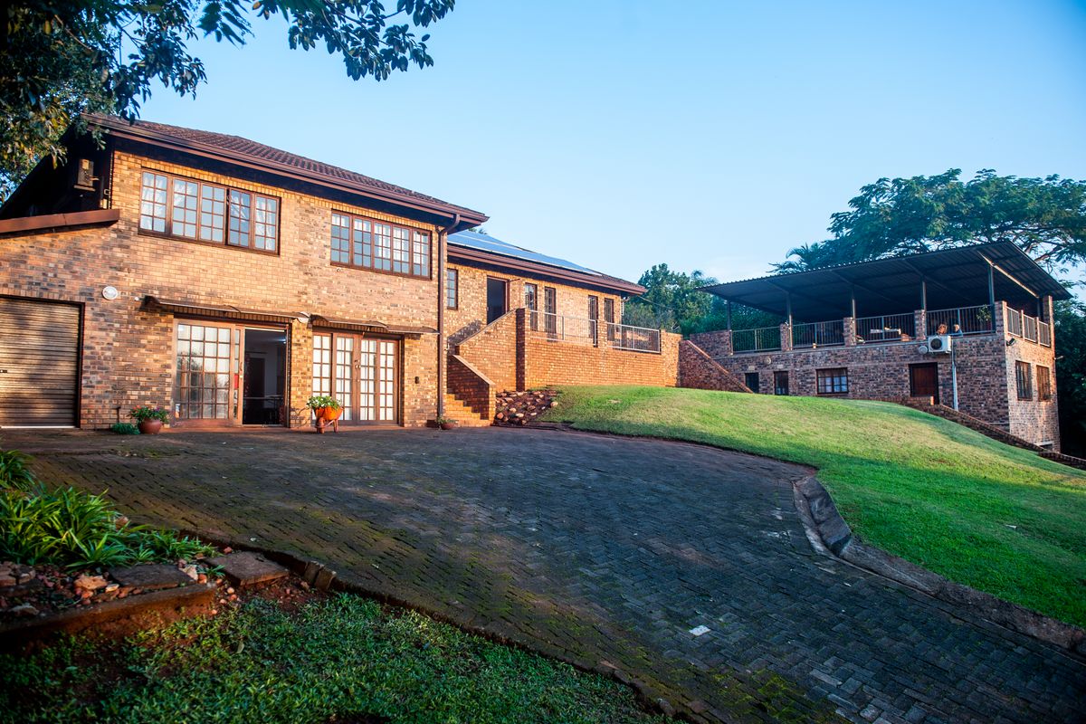 Spacious rear exterior view featuring a face brick house, paved driveway, and a raised patio area overlooking the garden.