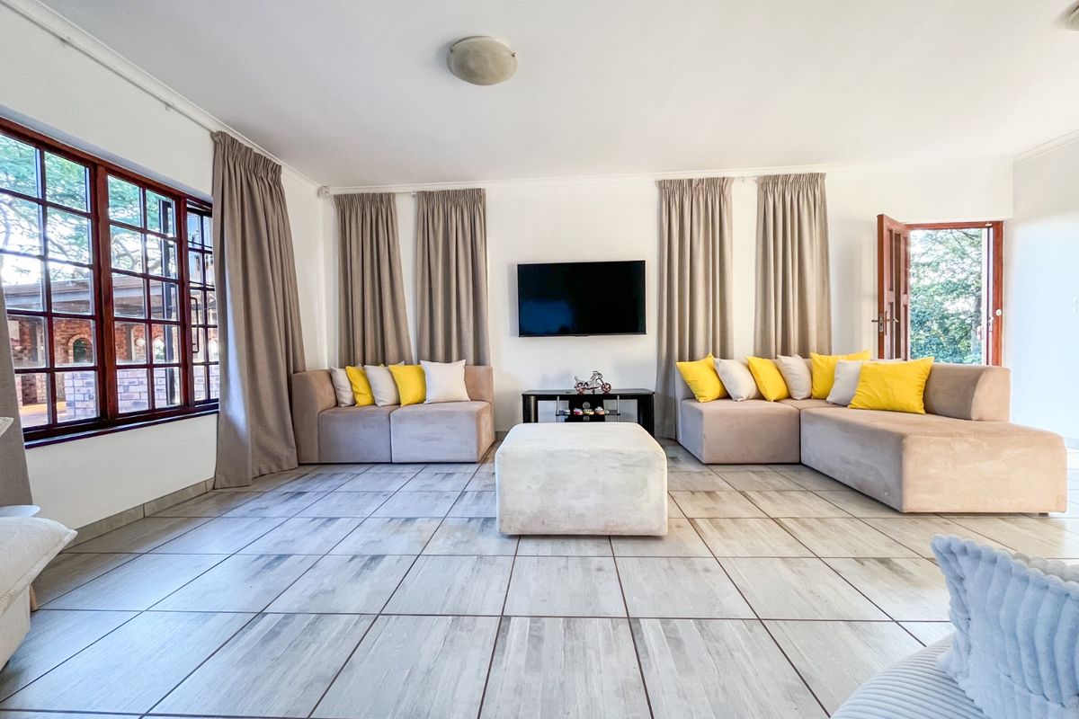 Spacious living room featuring light-toned tiled flooring, large timber-framed windows, and direct access to the outdoor area.