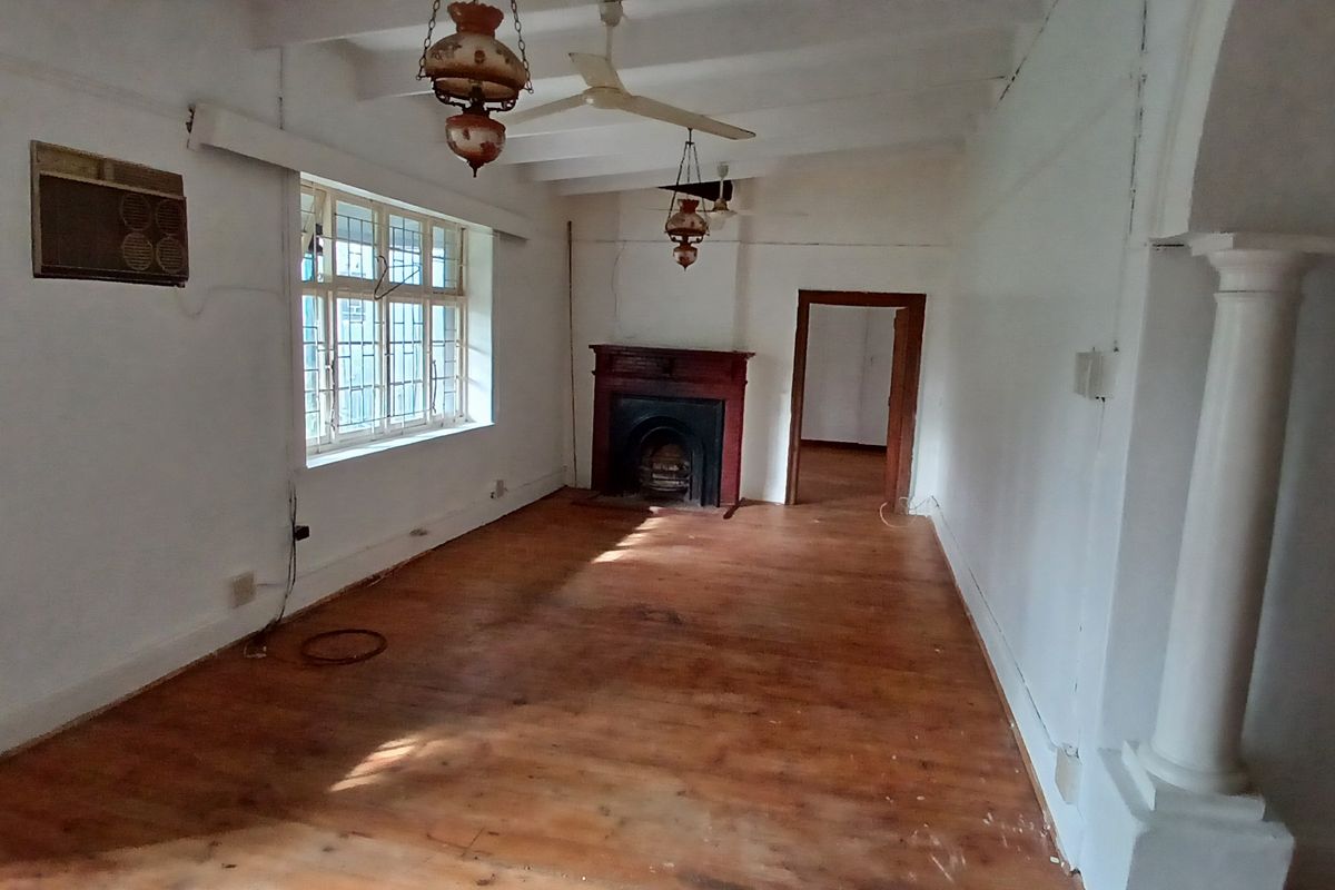 A spacious, empty living room featuring original timber flooring, a traditional fireplace, and classic architectural details including a decorative column.