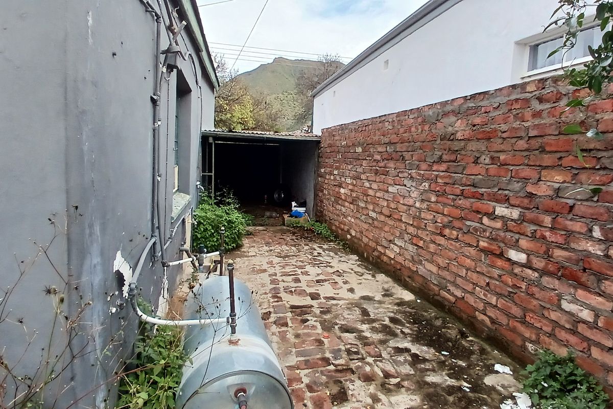A narrow side alleyway featuring exposed brick boundary walls, paved flooring, and an external water heating unit.