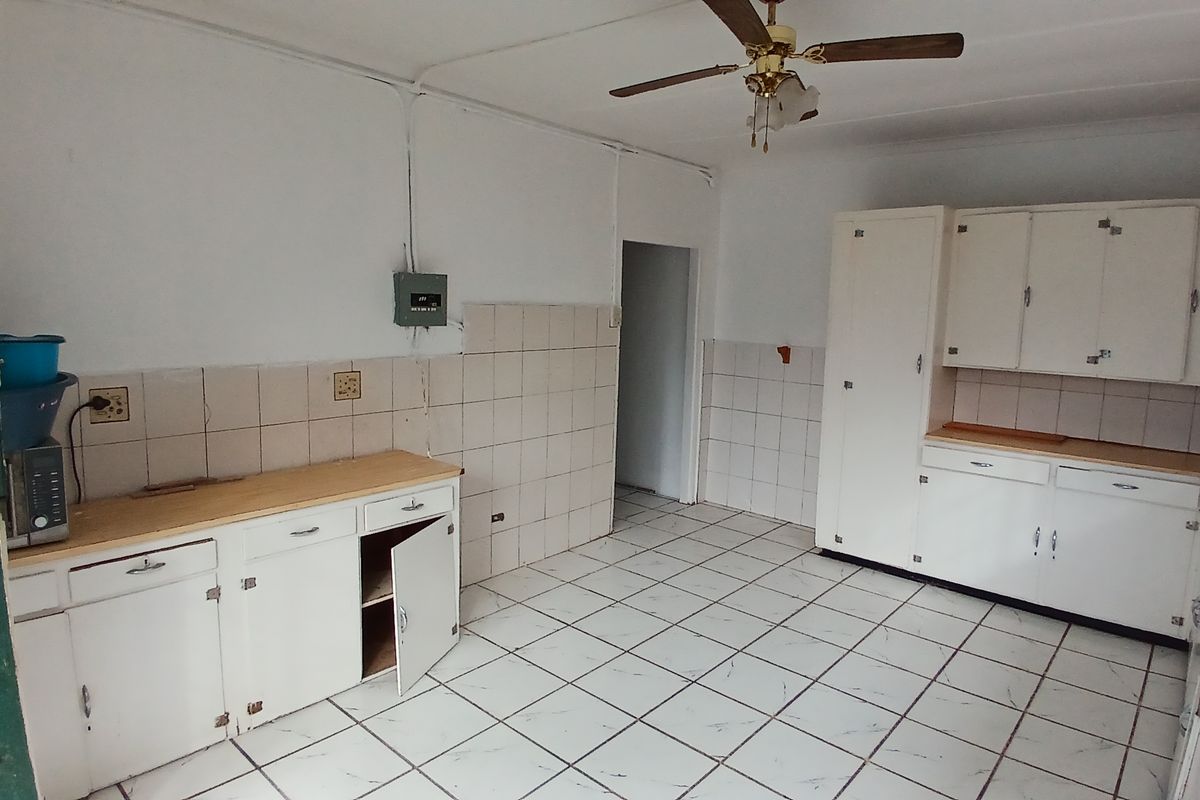 A dated kitchen featuring white cabinetry, tiled flooring, and tiled splashbacks, offering a functional layout ready for modernization.