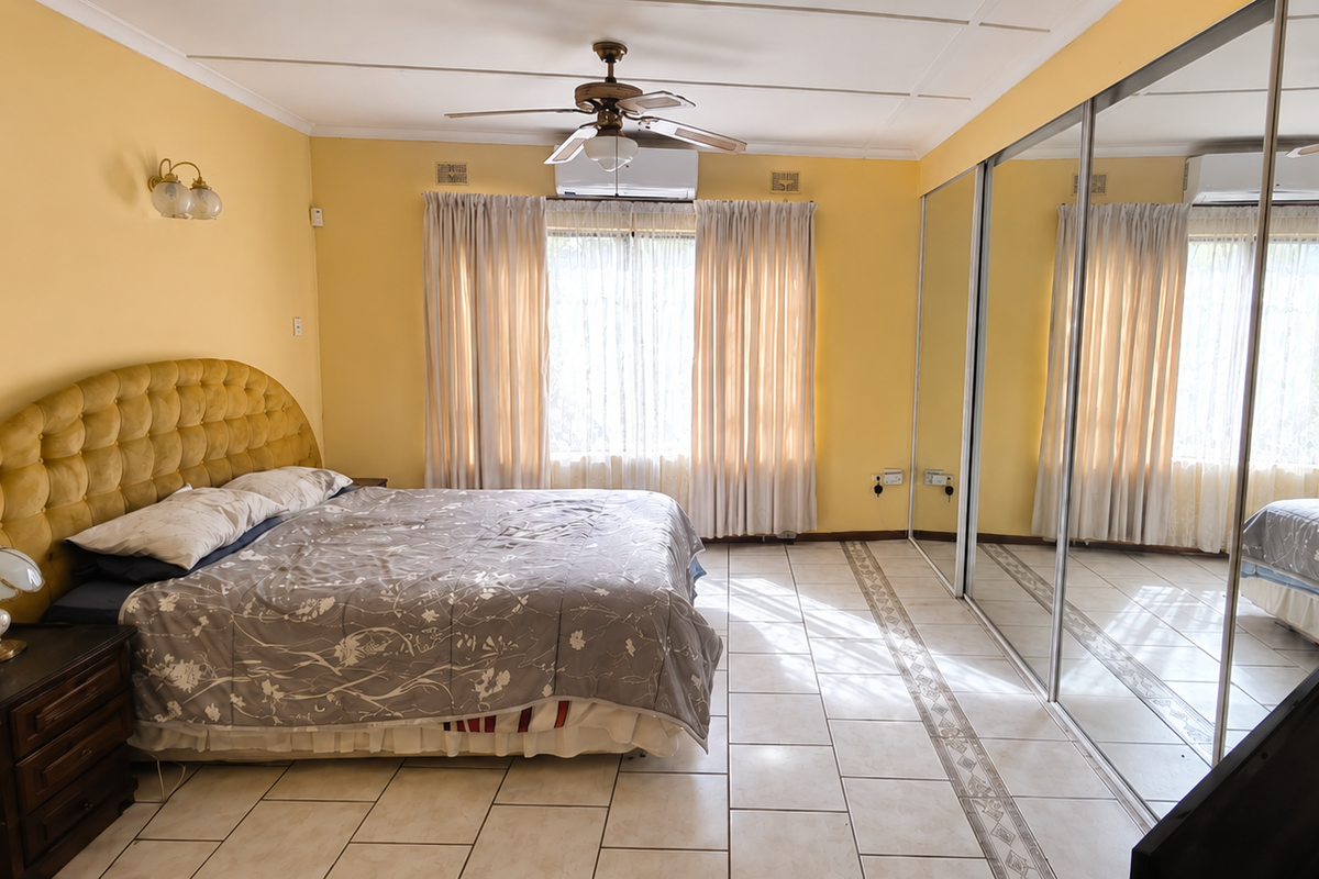 Spacious bedroom featuring large mirrored built-in cupboards, tiled flooring, a ceiling fan, and a wall-mounted air conditioning unit.