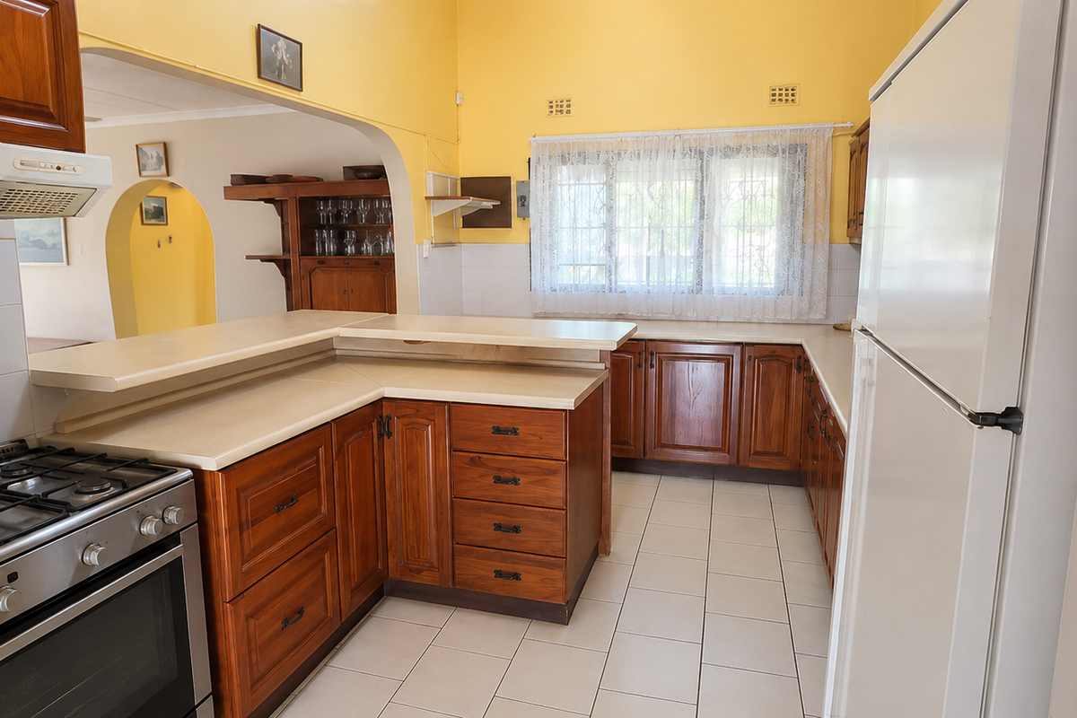 A functional kitchen featuring wooden cabinetry, a built-in gas stove with extractor fan, and tiled flooring, opening into an adjacent living area.