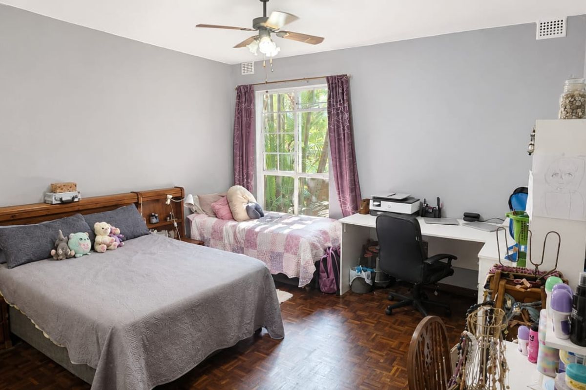 A spacious bedroom featuring parquet flooring, a ceiling fan, and a large window providing natural light and garden views.