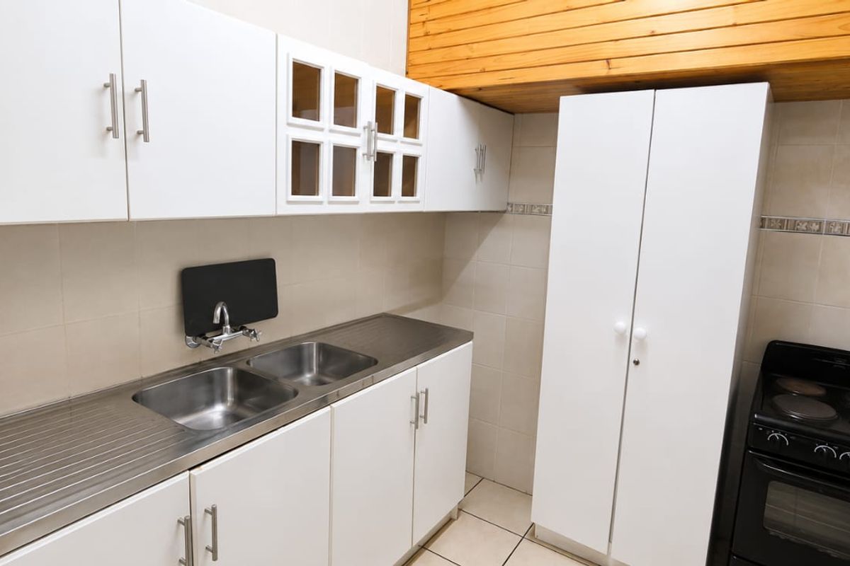 Functional kitchen featuring white cabinetry, stainless steel double sink, tiled splashbacks, and a freestanding electric stove.