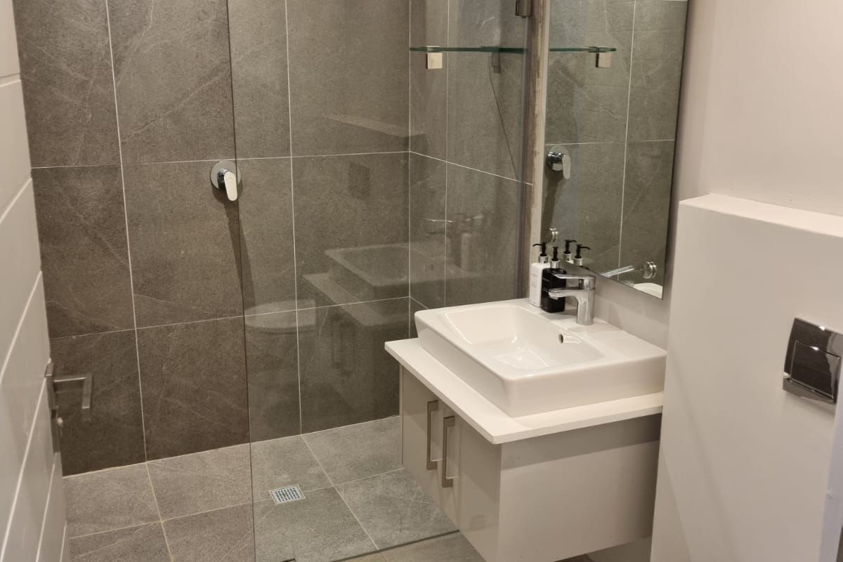 Modern bathroom featuring a walk-in shower with grey stone-look tiling, a wall-mounted vanity with a basin, and a concealed cistern toilet.