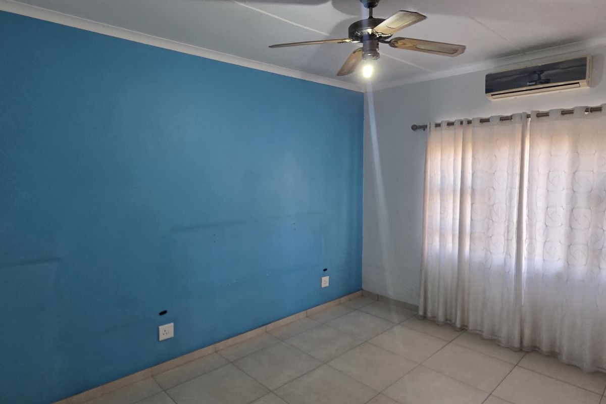 An empty bedroom featuring tiled flooring, a ceiling fan, and a wall-mounted split-system air conditioner.