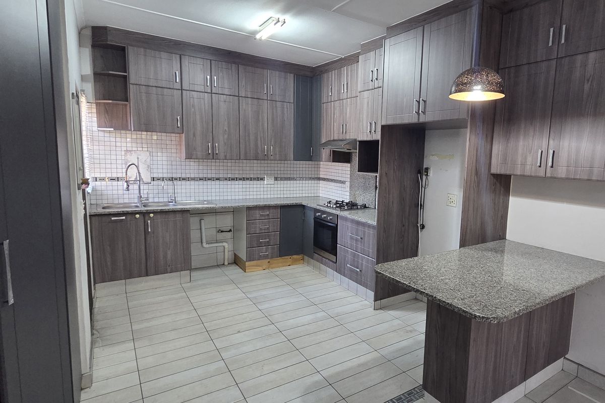 A functional kitchen featuring dark wood-grain cabinetry, granite countertops, a gas hob, and an integrated breakfast nook, ready for personal finishing touches.