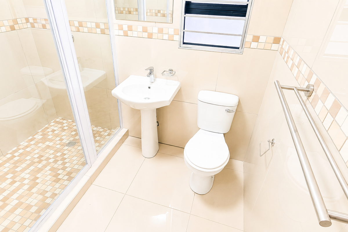 A clean, functional bathroom featuring a glass-enclosed shower, pedestal basin, and toilet with neutral wall and floor tiling.