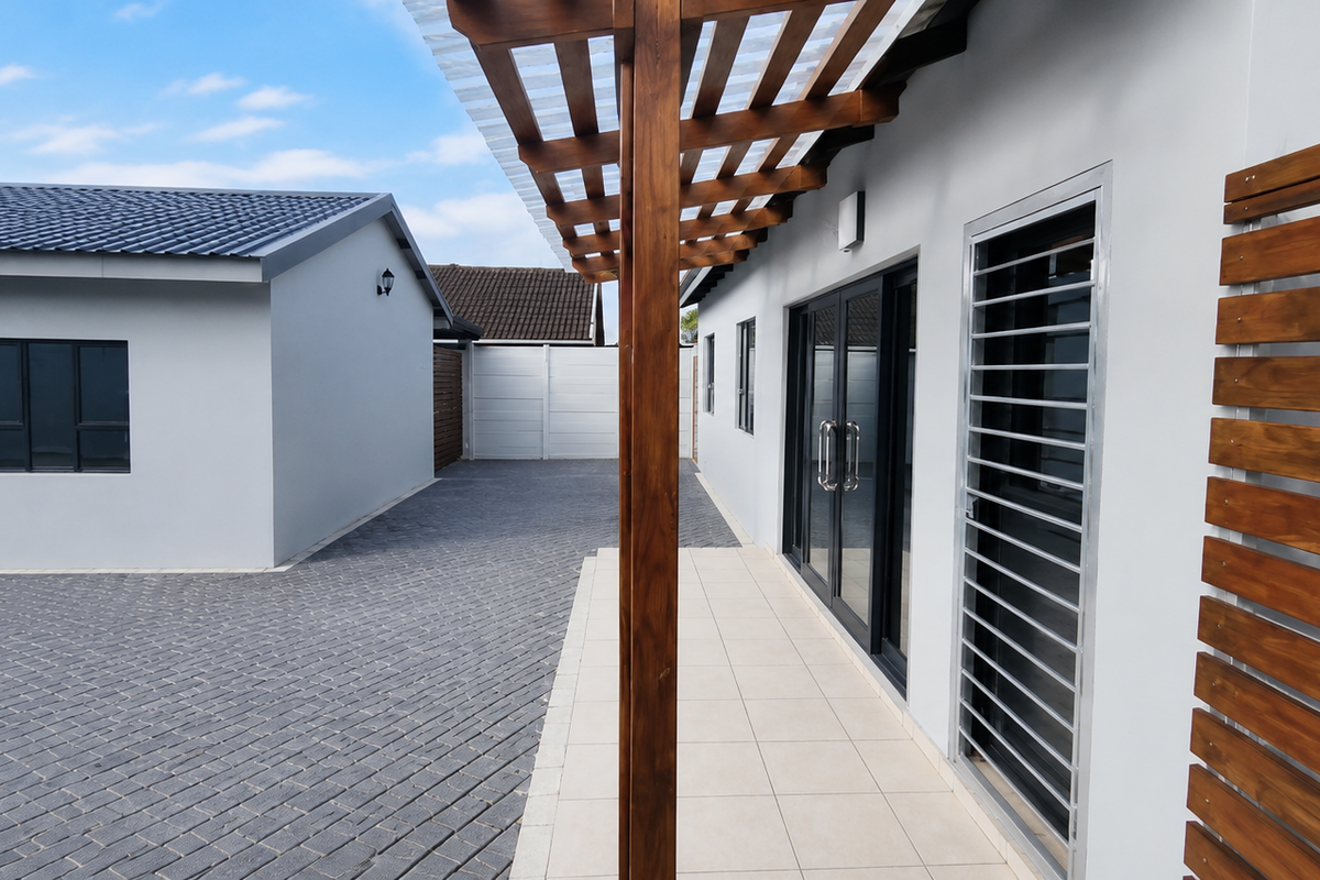 A well-maintained exterior view featuring a paved driveway, a covered patio with timber pergola, and modern grey-toned building facades.