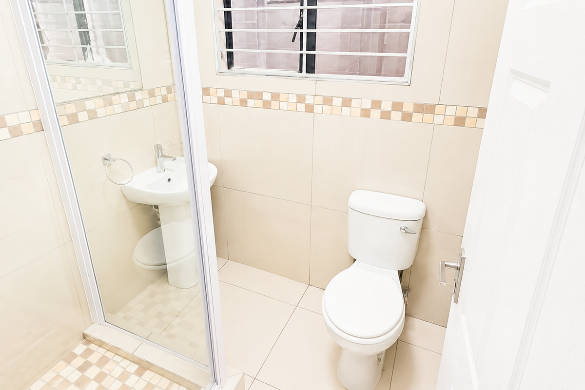 A compact bathroom featuring a glass-enclosed shower, pedestal basin, and toilet, finished with neutral wall and floor tiling.