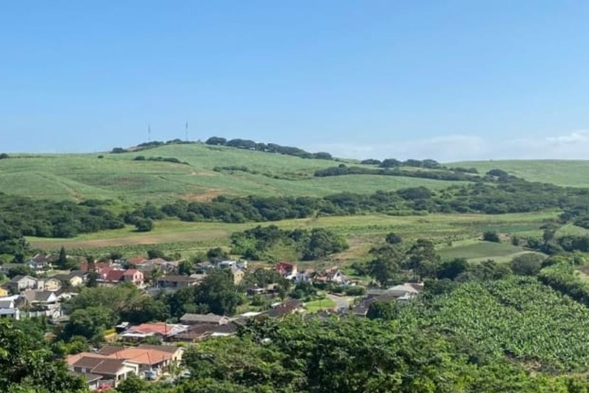 A scenic elevated view overlooking a residential neighborhood surrounded by lush green hills and agricultural land.