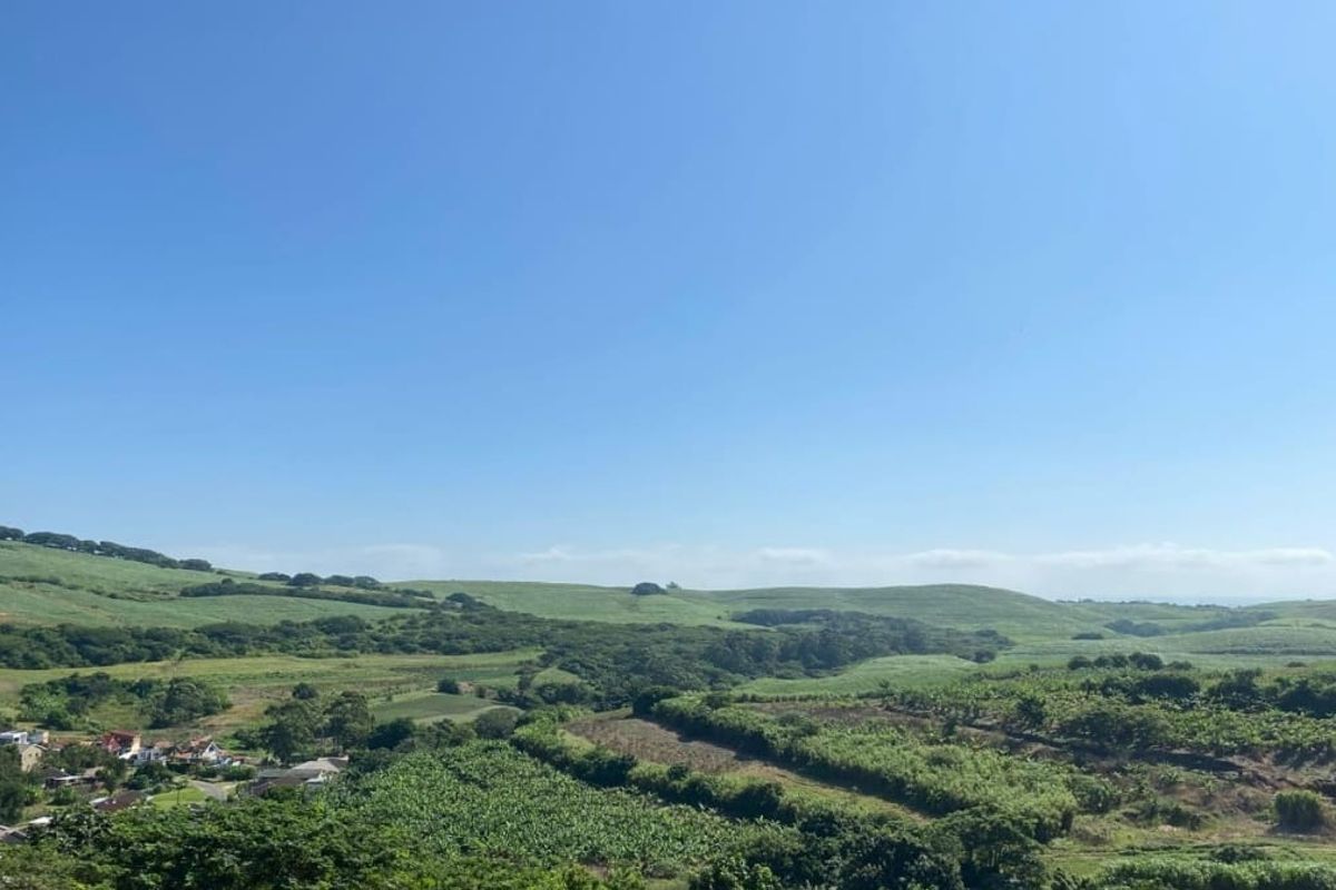 A scenic, elevated view overlooking expansive green hills, agricultural land, and distant residential properties under a clear blue sky.