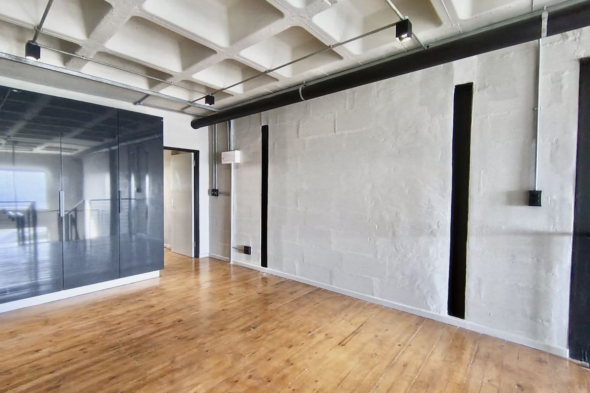 Spacious bedroom featuring industrial-style exposed waffle slab ceiling, polished timber flooring, and sleek built-in cabinetry.
