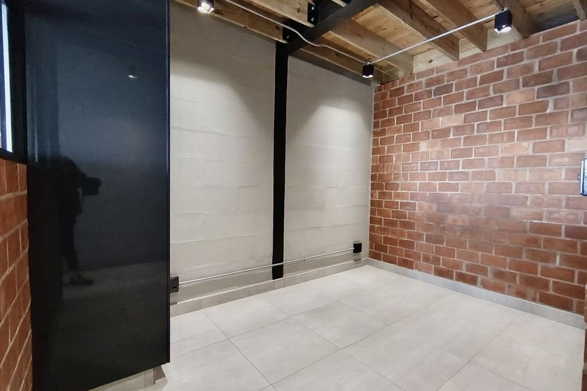 An empty room featuring industrial-style exposed brick walls, tiled flooring, and an exposed timber ceiling with track lighting.