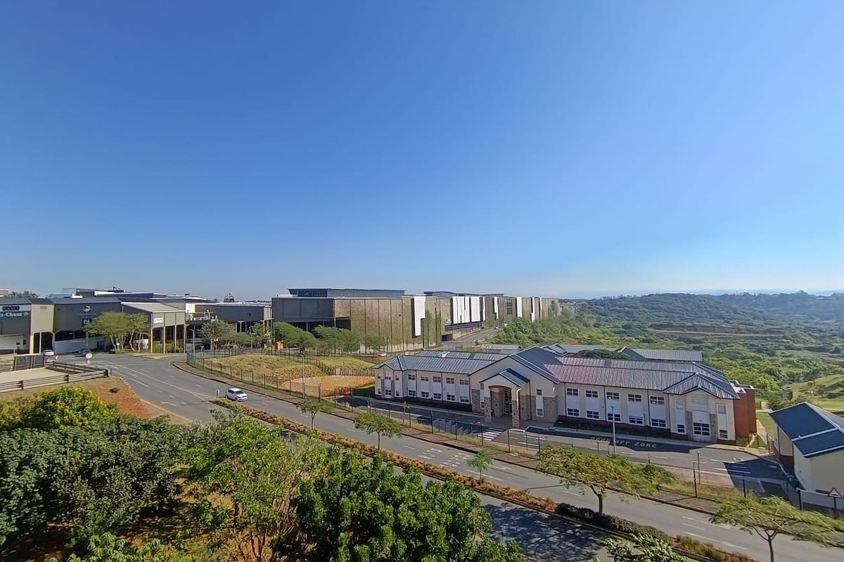 An elevated aerial view of the apartment complex surroundings, featuring nearby commercial buildings, landscaped grounds, and access roads under a clear blue sky.