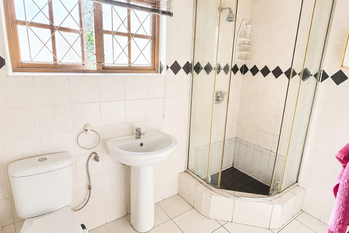 A functional bathroom featuring a pedestal basin, a corner shower enclosure with glass doors, and tiled walls with a decorative border.