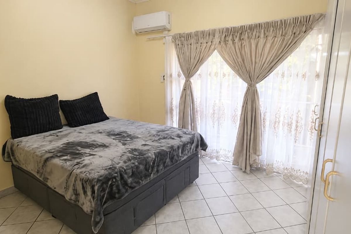 A bedroom featuring tiled flooring, a wall-mounted air conditioning unit, and built-in cupboards with access to a balcony through sliding glass doors.
