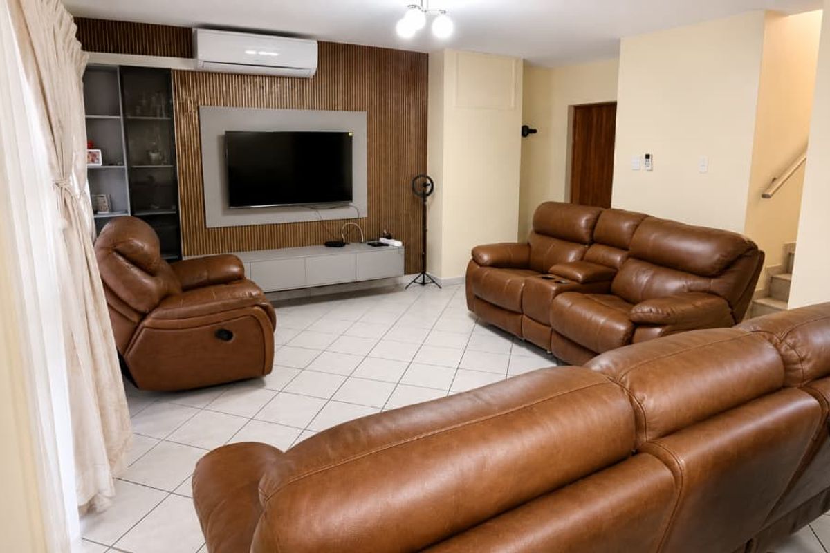 Spacious living area featuring tiled flooring, a decorative timber-slat feature wall, and a wall-mounted air conditioning unit.