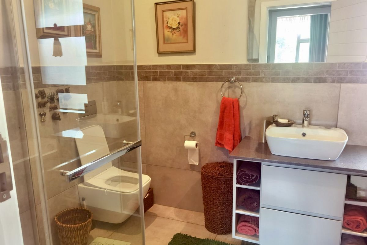 A functional bathroom featuring a glass shower enclosure, wall-mounted toilet, and a modern vanity with a vessel sink and large mirror.