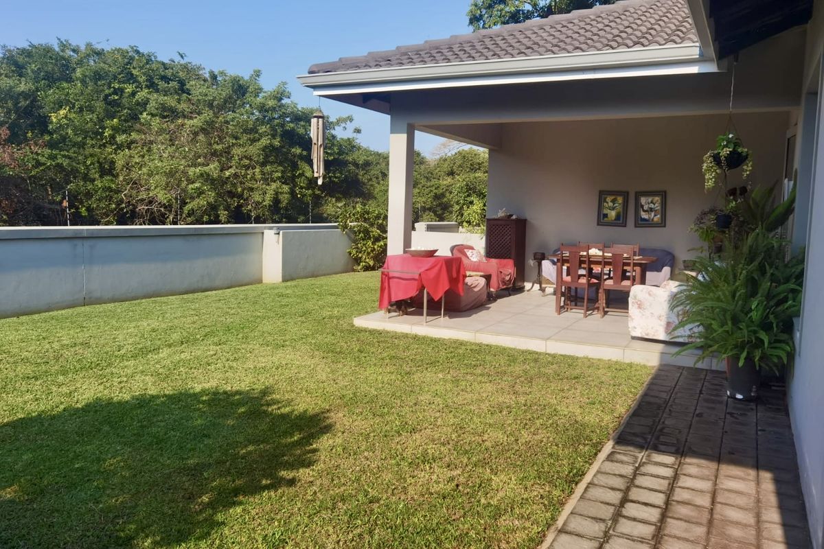 A covered patio area overlooking a private garden with a well-maintained lawn and concrete boundary wall.