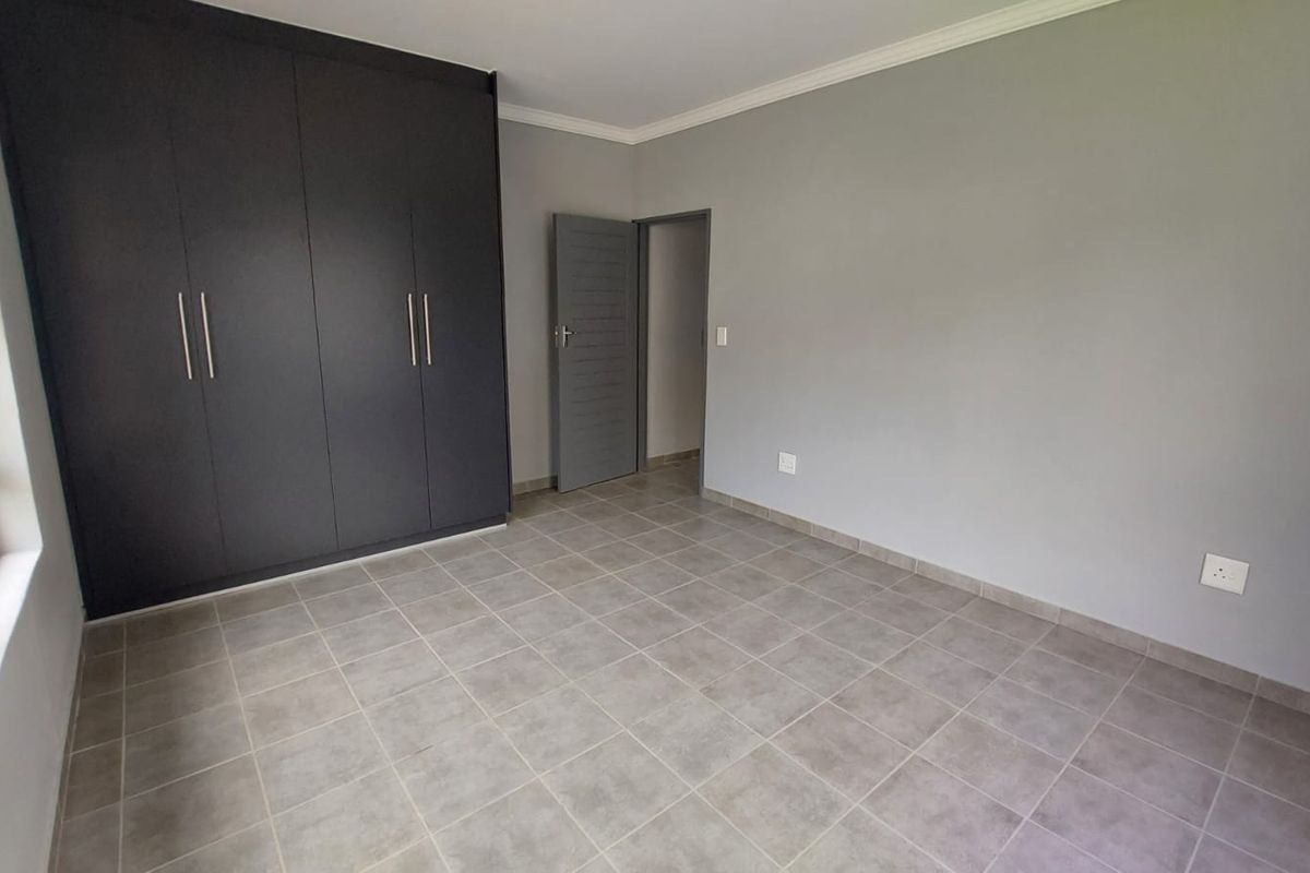 A clean, empty bedroom featuring neutral grey walls, tiled flooring, and modern dark built-in cupboards.