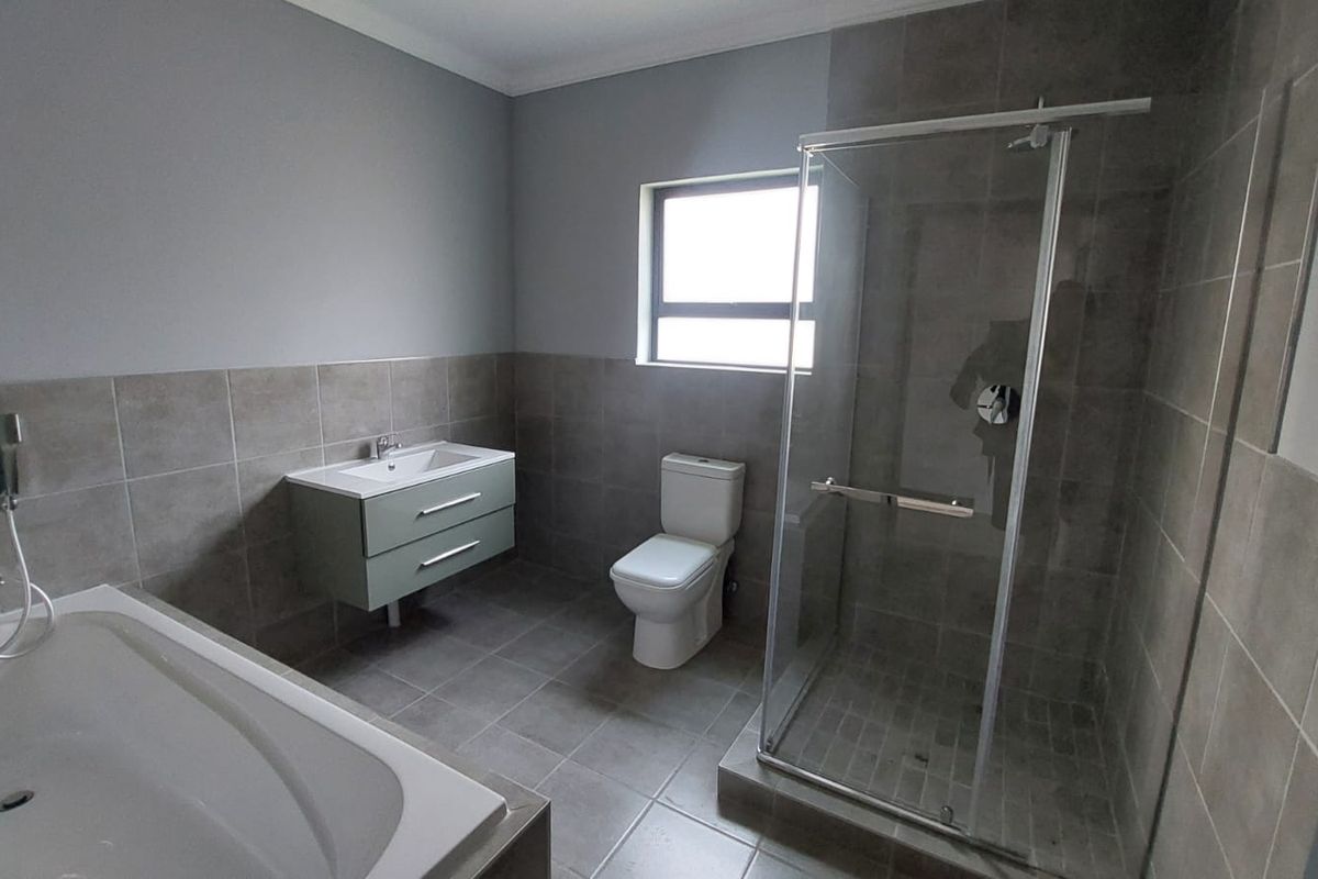 Modern bathroom featuring a wall-mounted vanity, a separate glass-enclosed shower, and a built-in bathtub with neutral floor-to-ceiling tiling.