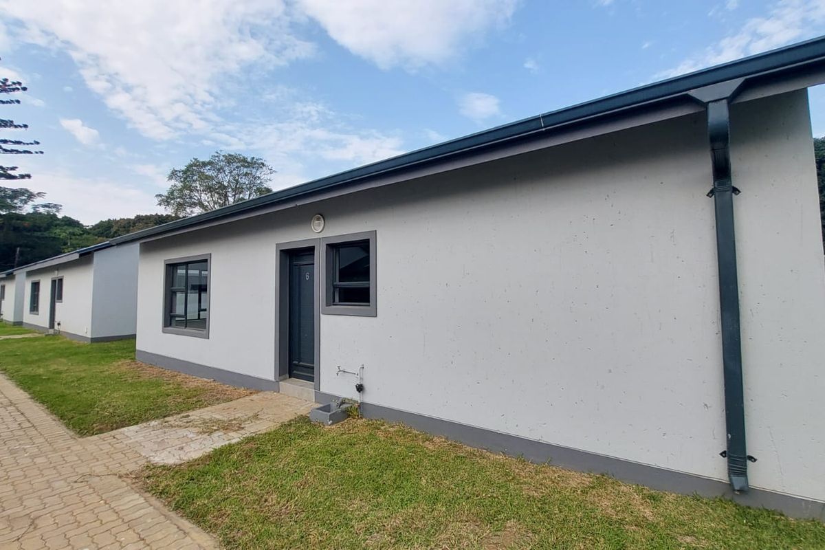 A view of the exterior rear facade of the townhouse, featuring a paved walkway, lawn, and modern grey-trimmed window and door frames.