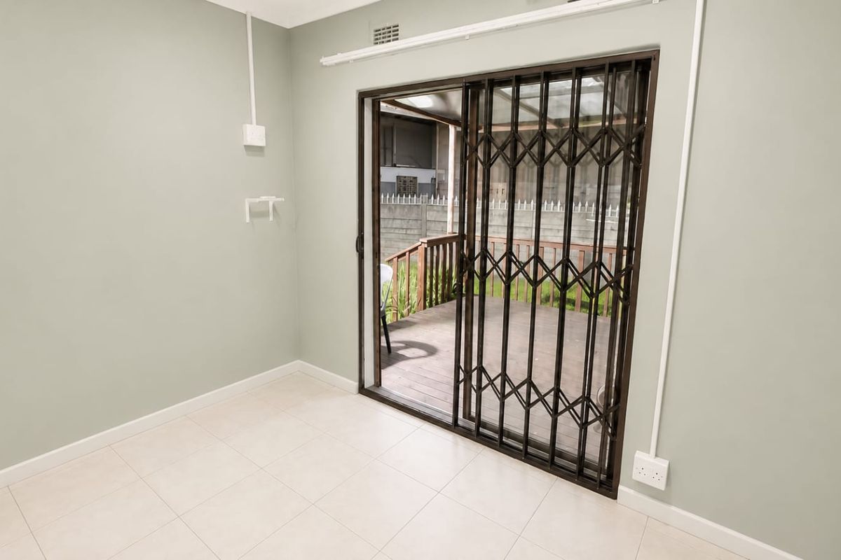 An empty living area featuring light-colored floor tiles and a sliding glass door with a security gate leading to an outdoor deck.