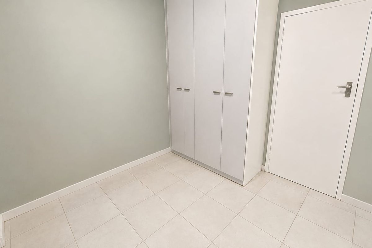 A clean, empty bedroom featuring neutral wall paint, light-colored tiled flooring, and a modern built-in wardrobe.