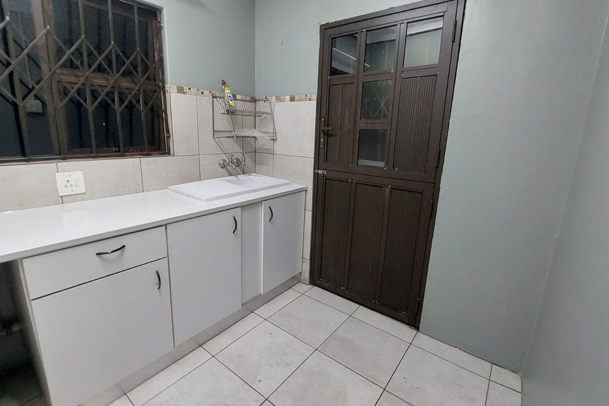 A functional laundry area featuring built-in white cabinetry, a sink, tiled backsplash, and direct access to an exterior door with security gate.