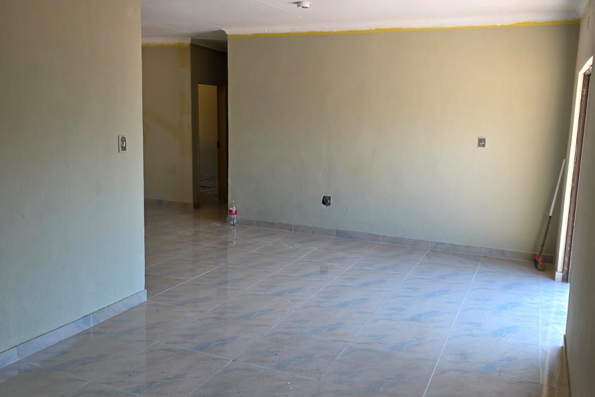 An empty, open-plan living area featuring tiled flooring and coved ceilings, currently undergoing minor finishing works.