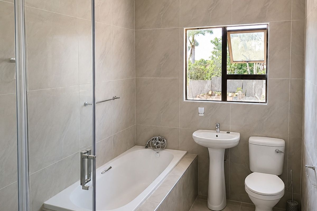 Modern bathroom featuring a built-in bathtub, separate glass shower enclosure, pedestal basin, and toilet with neutral floor-to-ceiling tiling.