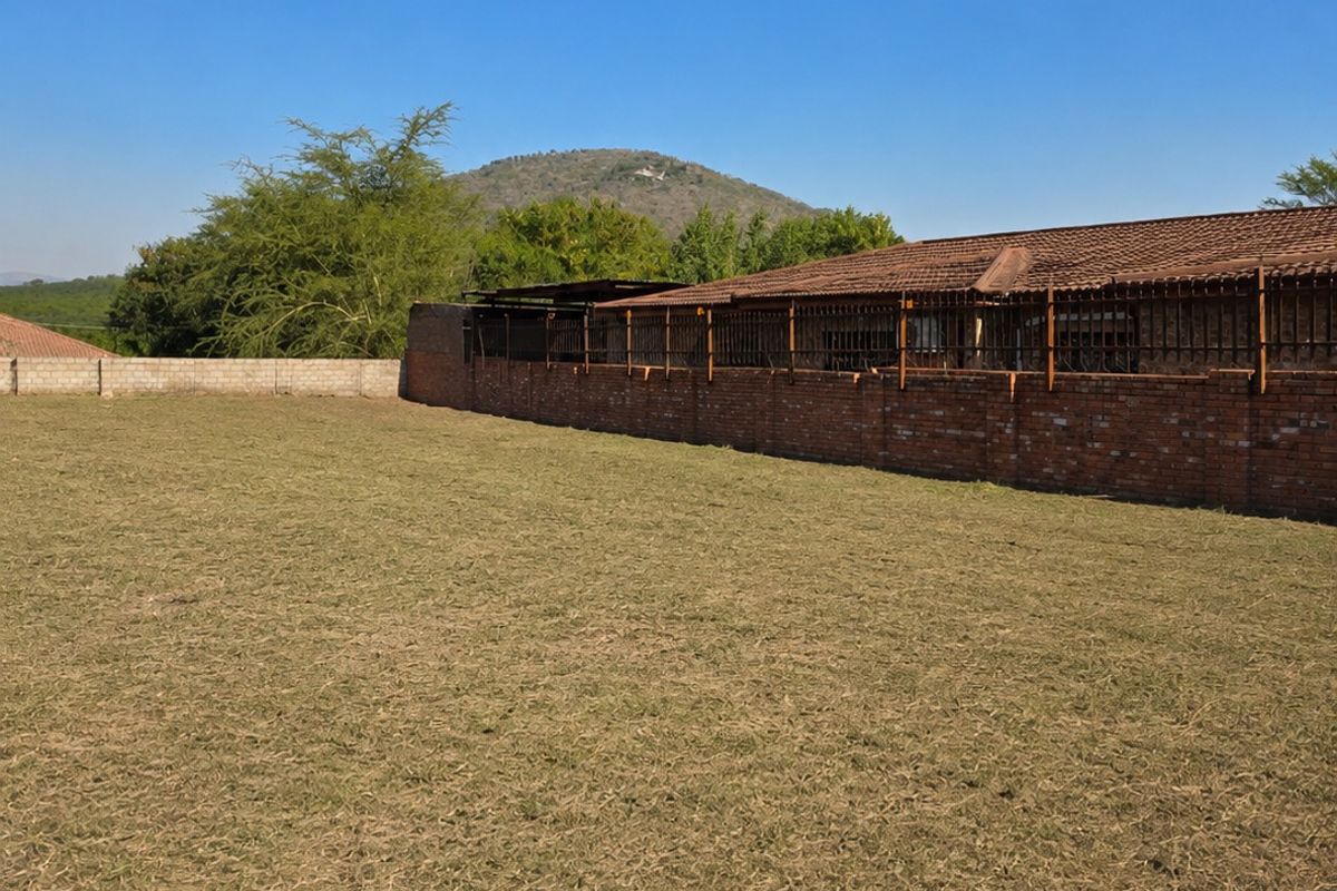 A spacious, level residential plot featuring a grass lawn enclosed by a brick boundary wall with integrated metal security fencing.