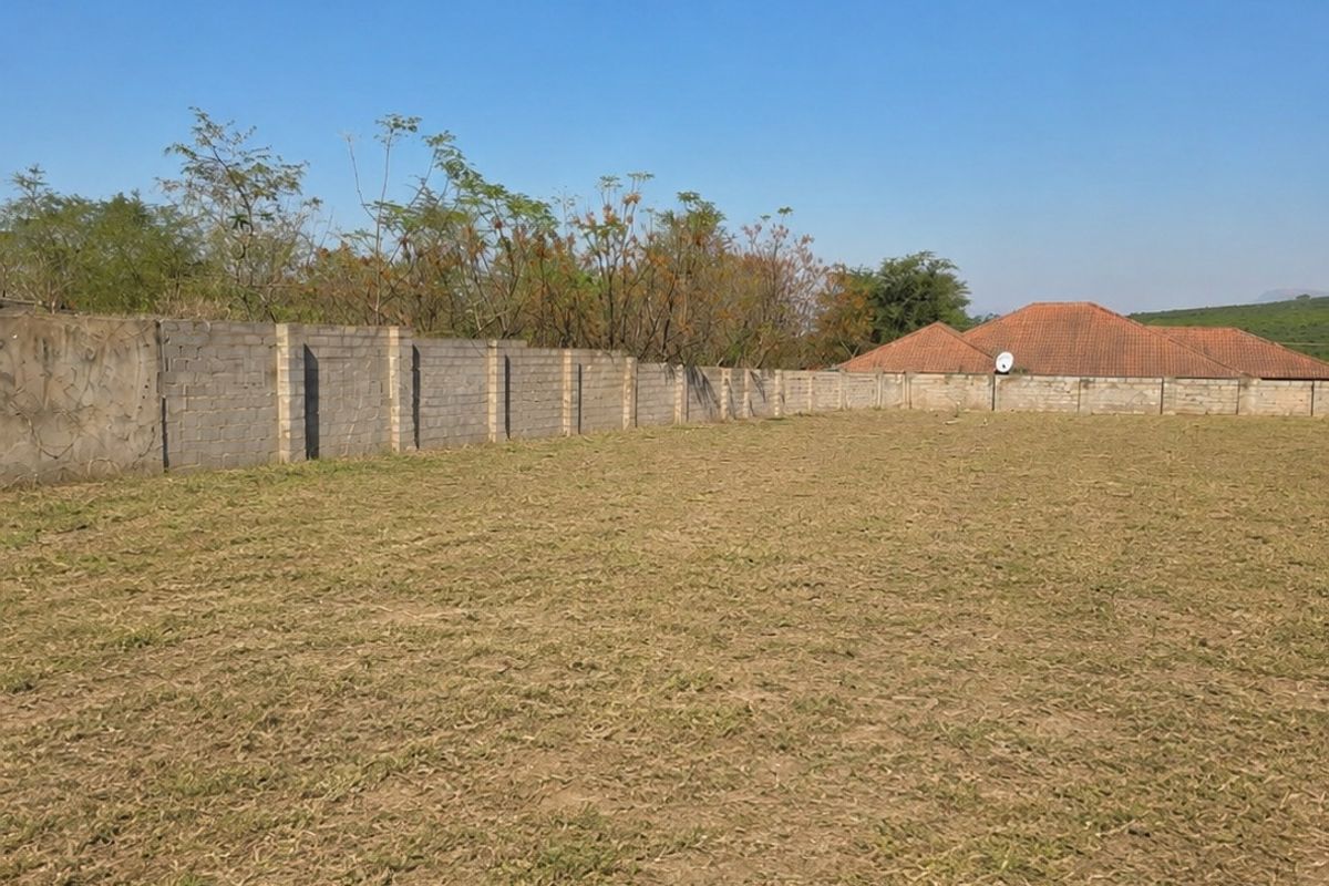 A vacant residential plot featuring a level grassed area enclosed by a concrete block perimeter boundary wall.